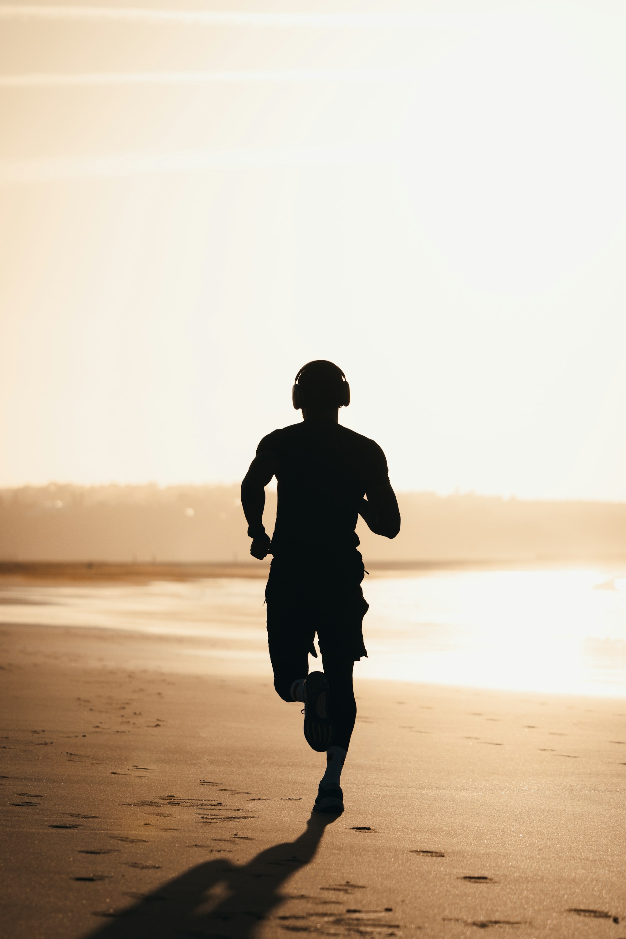 Runner crossing a beach at sunset with headphones